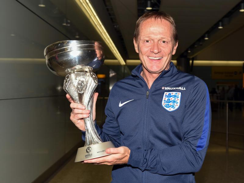 Keith Downing, der Trainer von Englands U19-Fußball-Nationalmannschaft zeigt den Pokal auf dem Flughafen Heathrow in London