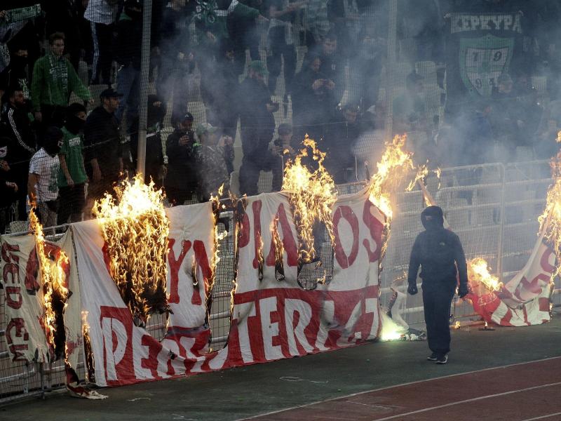 Vermummte Fans verbrennen während des Derbys ein Banner vor den Zuschauertribünen
