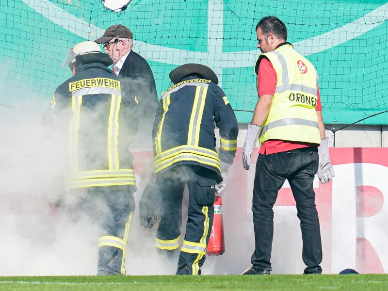 Feuerwehrleute löschen brennende Bengalos, die von Mainzer Fans aufs Spielfeld geworfen wurden