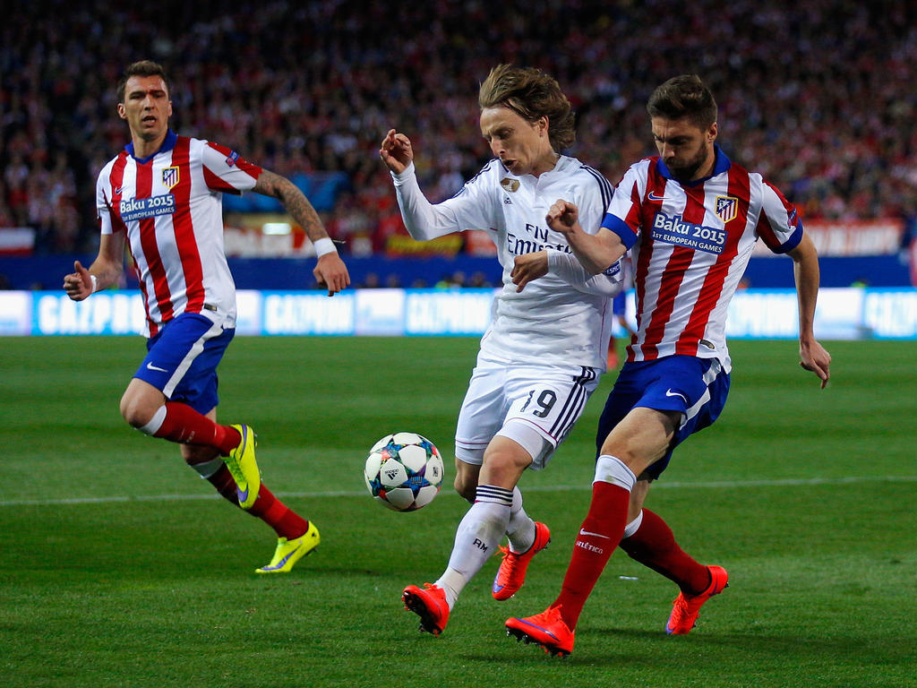 Luka Modrić (m.) gaat het lichaamsduel aan met Siqueira tijdens de Champions League-wedstrijd Atlético Madrid - Real Madrid. De spits Mario Mandžukić kijkt toe. (14-04-2015)