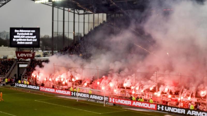 Fans brennen beim Derby zwischen dem FC St. Pauli und dem Hamburger SV Pyrotechnik ab, während eine Anzeigetafel genau davor warnt