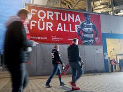 Zuschauer gehen im Stadion an einem Transparent mit der Aufschrift "Fortuna für alle" vorbei