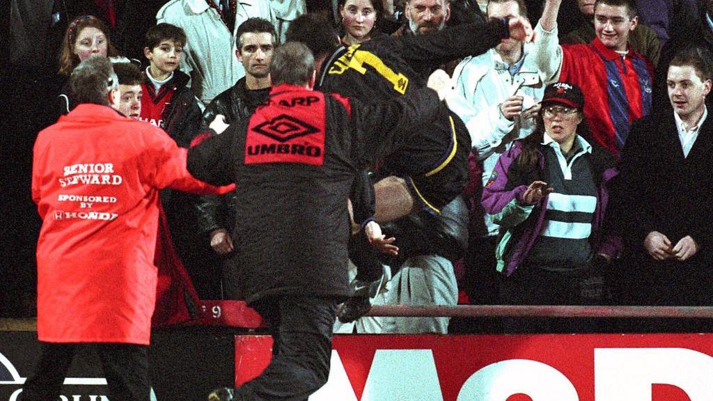 1995 springt Manchester Uniteds Éric Cantona (M.) über die Absperrung und tritt einen Fan um