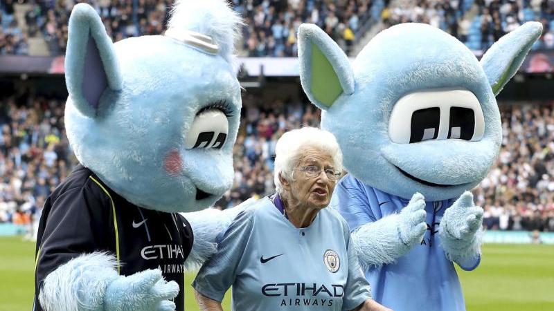Die 102 Jahre alte Vera Cohen wird von zwei Maskottchen vom Spielfeld geleitet