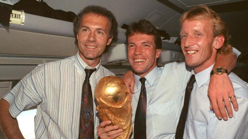 Auf dem Rückflug von Rom präsentieren DFB-Teamchef Franz Beckenbauer (l.), Kapitän Lothar Matthäus (M.) und Andreas Brehme den WM-Pokal