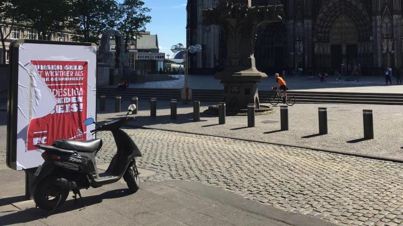 Ein halb abgerissenes Plakat hängt an einer Werbefläche vor dem Kölner Dom