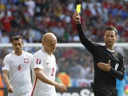 Scheidsrechter Mark Clattenburg (r.) geeft een gele kaart aan Polen-verdediger Michal Pazdan (m.), die over de schreef gaat in de achtste finale-wedstrijd tegen Zwitserland. (25-06-2016)