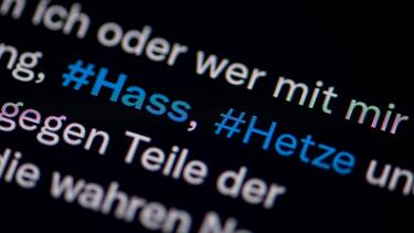 Auf dem Bildschirm eines Smartphones sieht man die Hashtags Hass und Hetze in einem Twitter-Post.