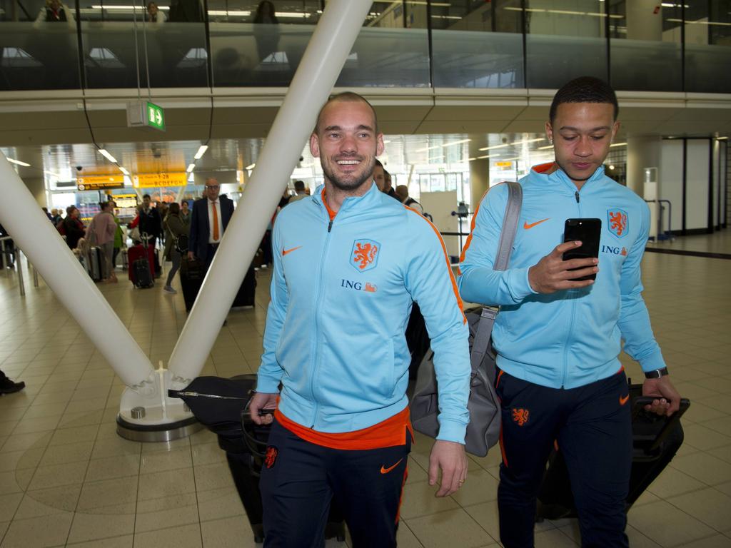 Terwijl Memphis Depay (r.) nog even op zijn telefoon kijkt, glimlacht Wesley Sneijder (l.) vlak voor vertrek naar Bulgarije nog even naar de pers. (24-03-2017)