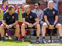 René Hake (l.) en Alfred Schreuder (m.) overleggen met elkaar op de bank bij FC Twente, terwijl Theo Pahlplatz naar het oefenduel met Team Twenterand kijkt. (11-07-2015)
