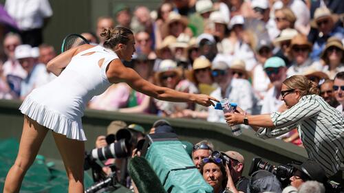 Aryna Sabalenka reicht eine Flasche Wasser und ein Kühlpack auf die Tribüne