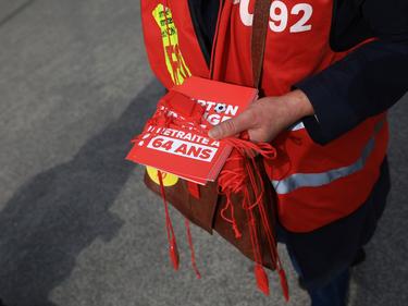 Ein Mitglied einer Gewerkschaft verteilt vor dem Spiel rote Karten mit der Aufschrift "Nein zur Rente mit 64 Jahren"